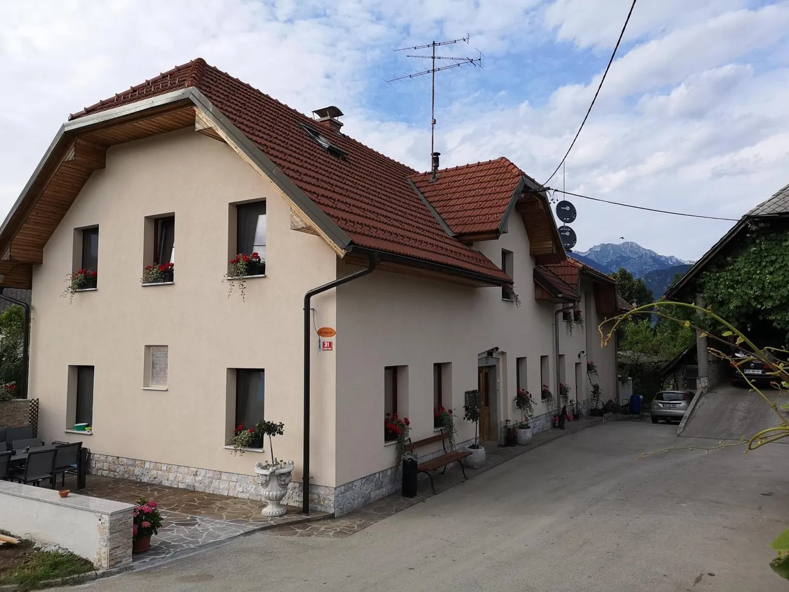 Hiša Apartmajev Bernard z rdečo streho in geranijami na oknih, za njo gore