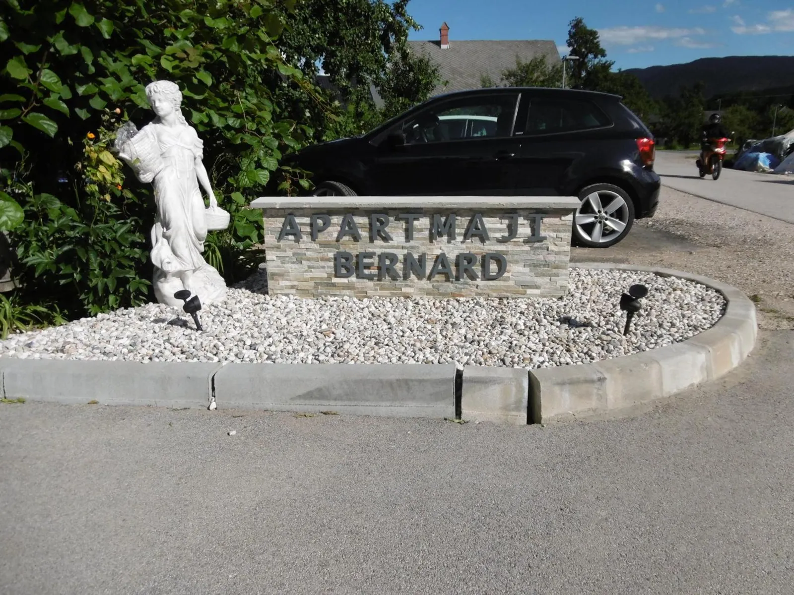 Kamnita tabla z napisom Apartmaji Bernard in kip ob vhodu na dvorišče